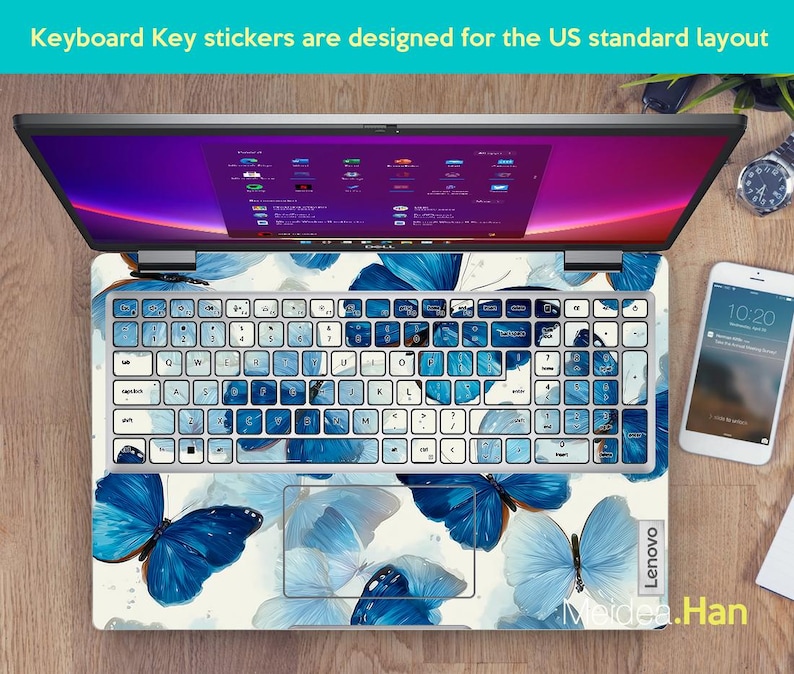 May include: Laptop with a keyboard overlay featuring blue butterfly designs. The keyboard keys are white with blue accents. The laptop screen displays a purple and pink interface. A smartphone and watch are visible.