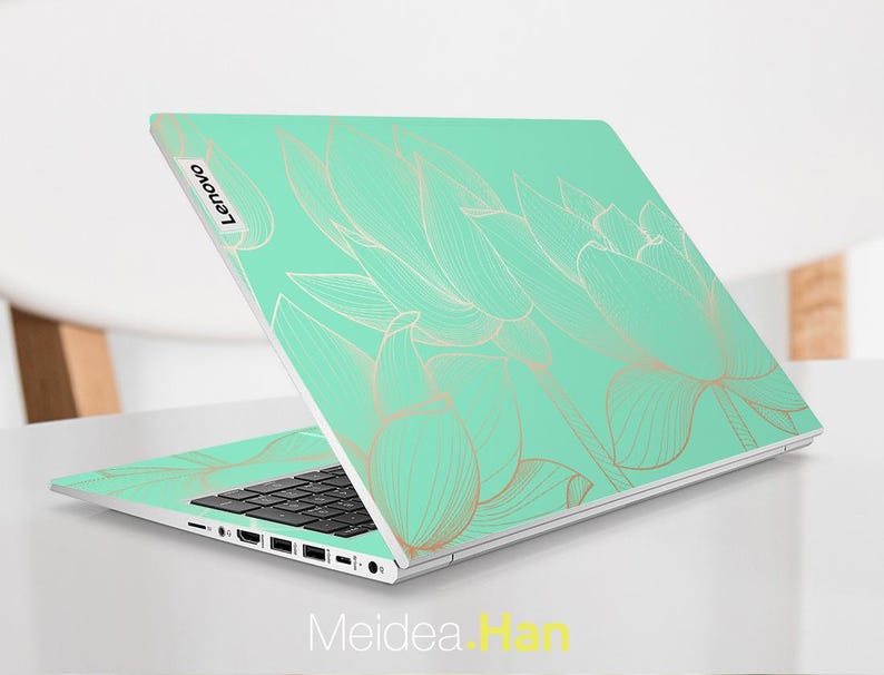 May include: A silver laptop with a mint green and gold floral design on the lid. The design features delicate, stylized lotus flowers. The laptop has a black keyboard and a silver trackpad. The Lenovo logo is visible on the lid.