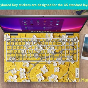 May include: A laptop computer with a yellow and white floral keyboard sticker. The sticker features a floral design with white flowers on a yellow background. The laptop is a Lenovo.