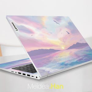 Pu&ograve; includere: Un laptop argentato con una scena di tramonto e oceano sul coperchio. La scena &egrave; dipinta in tonalit&agrave; di rosa, viola e blu. Il laptop ha una tastiera nera e un logo Lenovo sul coperchio.
