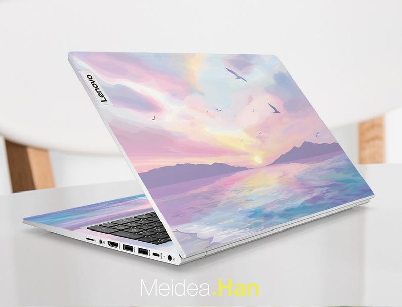 Pu&ograve; includere: Un laptop argentato con una scena di tramonto e oceano sul coperchio. La scena &egrave; dipinta in tonalit&agrave; di rosa, viola e blu. Il laptop ha una tastiera nera e un logo Lenovo sul coperchio.