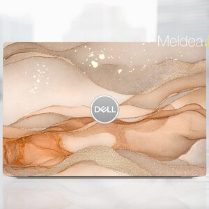 Puede incluir: Una piel para portátil con un diseño abstracto beige y marrón con detalles de purpurina dorada. El logotipo de Dell es visible en el centro de la piel.