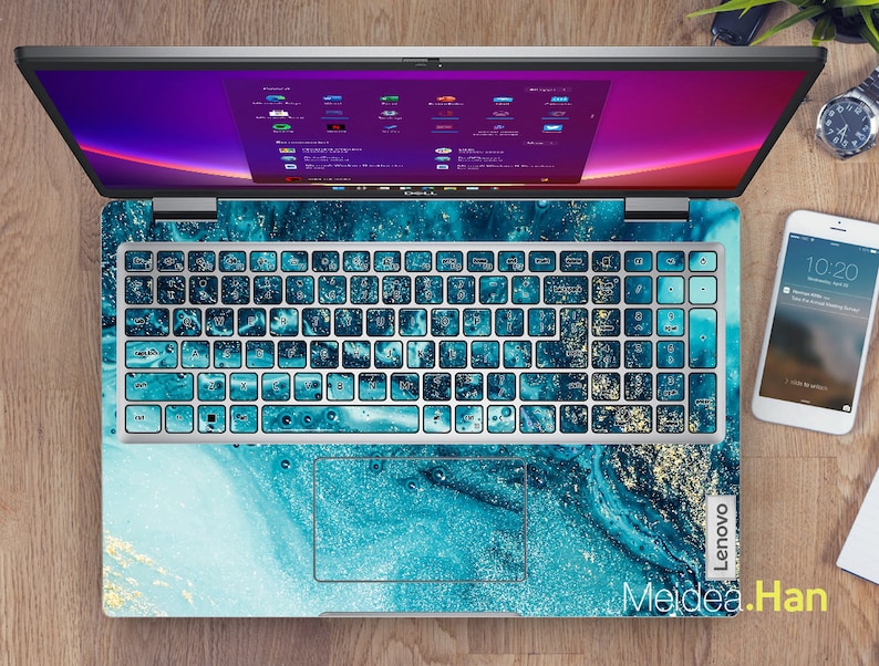 Op de afbeelding: Een laptop met een blauwe en gouden marmer-toetsenbordhuid. De huid heeft een blauw en gouden marmerpatroon op een witte achtergrond. De laptop is open en het scherm toont een bureaublad met verschillende pictogrammen. De laptop staat op een houten oppervlak.