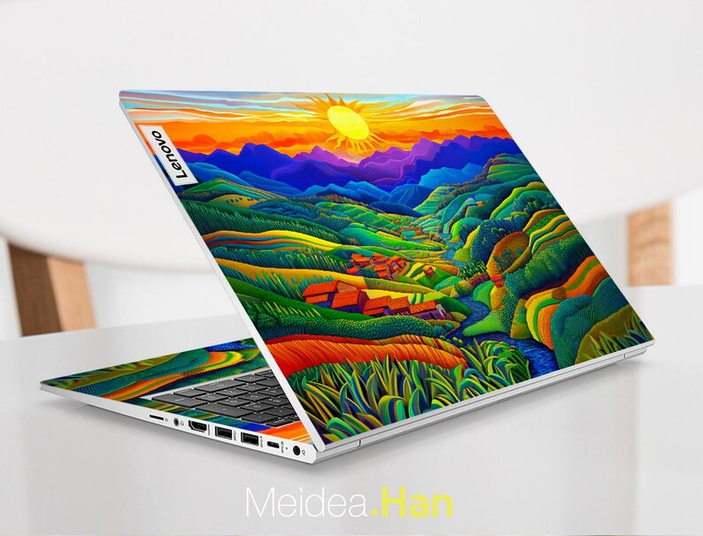 May include: A laptop computer with a colourful landscape design on the lid. The design features a sunset, mountains, and a river. The laptop is open and the keyboard is visible. The Lenovo logo is visible on the lid.