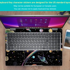 May include: A laptop computer with a black and white space-themed keyboard sticker. The sticker features planets, stars, and a rainbow. The text on the sticker reads "Keyboard Key character stickers are designed for the US standard layout. May not be suitable for European or Canada users. You can choose not to apply keyboard key stickers."