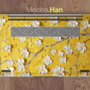 May include: A laptop skin with a yellow background and white flowers. The skin features a floral design with a textured look. The text "Meidea.Han" is printed on the skin.