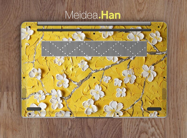 May include: A laptop skin with a yellow background and white flowers. The skin features a floral design with a textured look. The text "Meidea.Han" is printed on the skin.