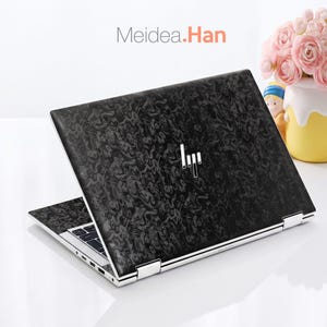 May include: A laptop featuring a black and grey marbled pattern skin on the lid and keyboard deck. The device displays a silver HP logo in the centre of the lid. The text Meidea.Han is visible above the laptop. The laptop is partially open.