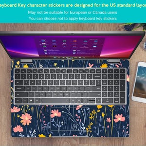 May include: A silver laptop computer with a floral design keyboard sticker. The laptop is open and the screen is displaying a desktop with multiple icons. The laptop is sitting on a wooden surface with a white smartphone and a watch.