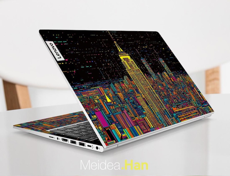 Pode incluir: Um laptop prateado com um design de cidade colorida na tampa. O design apresenta um pr&eacute;dio alto com um fundo preto e linhas coloridas. O laptop tem um teclado preto e um touchpad prateado. O logotipo da Lenovo &eacute; vis&iacute;vel na tampa.