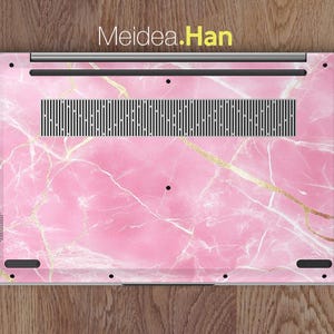 May include: Pink marble laptop skin with gold accents. The skin has a Meidea.Han logo on the top.