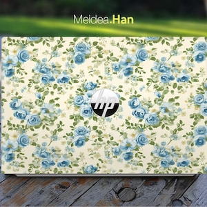May include: A laptop computer with a floral design skin. The design features blue and white flowers on a cream background. The HP logo is visible on the laptop.