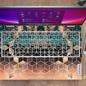 May include: A laptop computer with a geometric pattern keyboard cover in shades of gold, teal, and brown. The cover features a repeating pattern of hexagons and squares. The laptop screen is displaying a desktop with multiple icons.
