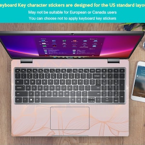 Puede incluir: Un port&aacute;til con un dise&ntilde;o floral rosa en el teclado y el &aacute;rea circundante. El teclado tiene pegatinas de caracteres de teclas dise&ntilde;adas para el dise&ntilde;o est&aacute;ndar de EE. UU. Tambi&eacute;n se ven un tel&eacute;fono inteligente y un reloj.