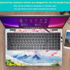 May include: A laptop computer with a keyboard and a touchpad. The laptop has a sticker on the keyboard and touchpad that features a mountain scene with pink cherry blossoms. The text on the screen reads "Windows 11 Home".