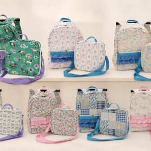 Könnte beinhalten: Eine Kollektion aus passenden Rucksack- und Lunchtaschen-Sets mit verschiedenen Blumen-, Pferde-, Schmetterlings- und Karomustern. Jedes Set enthält einen Rucksack mit Reißverschluss und Rüschen-Fronttasche sowie eine quadratische Lunchtasche.