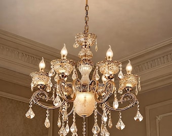 Pode incluir: Um lustre de vários braços com acabamento em latão antigo, volutas de metal ornamentadas e numerosos pingentes de cristal transparente. A luminária inclui seis lâmpadas tipo vela, uma taça central de vidro fosco e uma corrente de suspensão.