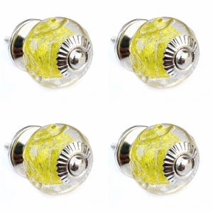 Puede incluir: Cuatro pomos de armario de vidrio transparente con detalles amarillos y plateados. Cada pomo tiene un centro redondo de vidrio transparente con remolinos amarillos, una base de metal plateado y un tornillo de metal plateado.