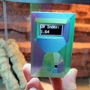 May include: A small, iridescent, 3D printed device with a digital display showing "UV Index: 1.64".