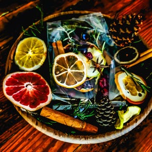 May include: A wooden tray filled with dried citrus slices, cinnamon sticks, pine cones, and sprigs of rosemary. The arrangement includes a half grapefruit, lemon slices, and a clear bag with dried fruit and berries. The tray sits on a wooden surface.