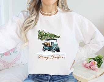 Może przedstawiać: Biała bluza z nadrukiem przedstawiającym wózek golfowy przewożący choinkę. Pod obrazkiem znajduje się napis "Merry Christmas".
