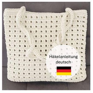 Może przedstawiać: Kremowa torba typu tote z otwartym splotem z szydełka z uchwytami z liny. Torba ma prostokątny kształt i szereg małych, równomiernie rozmieszczonych otworów w całym projekcie. Widoczna jest okrągła grafika z niemieckim tekstem i flagą.