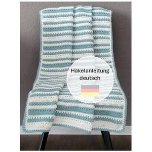 May include: A handmade, striped crochet blanket in shades of white and teal blue, draped over a chair. The blanket features a repeating horizontal stripe pattern. The image includes text in German.