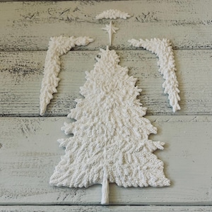 May include: A white Christmas tree and angel wing set, with a star and decorative elements. The tree is textured and detailed, with a trunk at the base. The wings are in two pieces, and the star is at the top.