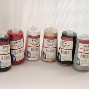 May include: Six spools of thread for an overlock sewing machine. The spools are in the colours black, red, white, beige, dark grey, and light grey. Each spool has a label that says "Birch Overlocking Thread 100% Cotton" and a barcode.