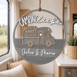 Könnte beinhalten: Ein rundes, graues Holzschild zum Aufhängen mit einer Wohnmobil-Illustration in der Mitte. Der Schriftzug "CAMPINGliebe" steht oben, "Julia & Marco" unten. Das Schild hängt an einem braunen Seil und hat vertikale Linien als Ausschnitte.