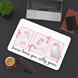 May include: White mousepad with a black border featuring three cartoon geese in pink frames. The geese have bows and flowers. The text "Jesus loves you, silly goose" is written in black script. A computer mouse rests on the pad.