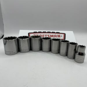 May include: A collection of eight silver metal sockets, each with a cylindrical body and a hexagonal opening. The sockets are of different sizes and are arranged in a row. Each is marked with numbers.