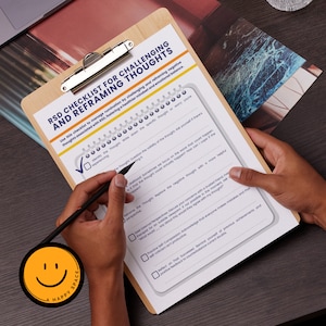 May include: A wooden clipboard with a checklist titled "RSD Checklist for Challenging and Reframing Thoughts." The checklist is being filled out with a black pen. A round sticker with a smiling face and the words "A Happy Space" is in the lower left corner.
