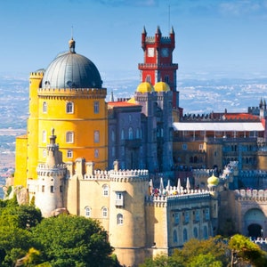 May include: A yellow and red castle with a large dome on top, set against a blue sky and a distant view of a city.