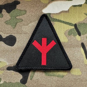 May include: A black triangular patch with a red symbol resembling a stylised tree or a Y shape.