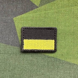 Könnte beinhalten: Ein gestickter schwarzer und gelber Aufnäher mit einem schwarzen Rechteck oben und einem gelben Rechteck unten.