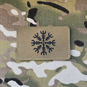 Może przedstawiać: Beige naszywka z haftowanym czarnym symbolem stylizowanej ośmiopromiennej gwiazdy z krzyżem w środku.