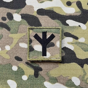 May include: A black and green camouflage fabric patch with a black symbol resembling a stylized tree or a Y shape.