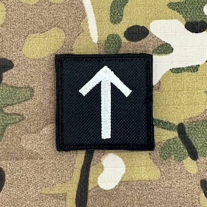 Peut inclure: Patch en tissu noir avec une flèche blanche pointant vers le haut.