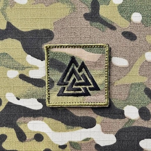 May include: A black embroidered patch with a triangular symbol on a camouflage background. The symbol is a stylized triangle with three interlocking triangles inside.