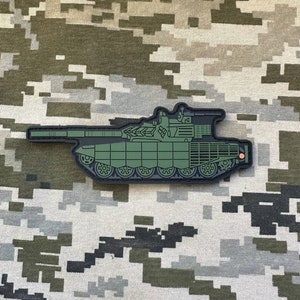 Könnte beinhalten: Ein grüner und schwarzer Militär-Patch mit einem Panzer. Der Panzer ist nach rechts gerichtet und hat einen langen Lauf. Der Patch ist aus strapazierfähigem Material gefertigt und perfekt, um Ihren Kleidungsstücken oder Ihrer Ausrüstung einen Hauch von Militärstil zu verleihen.