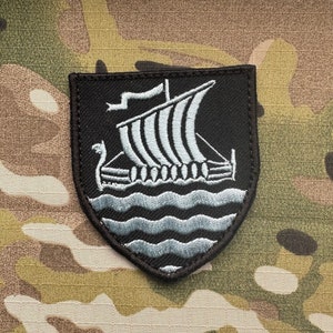 May include: A black embroidered patch featuring a white ship and waves. The ship has a sail and oars. The patch is shaped like a shield.