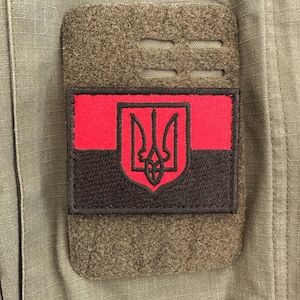 Może przedstawiać: Naszywka haftowana w kolorze czarnym i czerwonym z ukraińskim herbem, trójzębem, na zielonym tle z tkaniny.