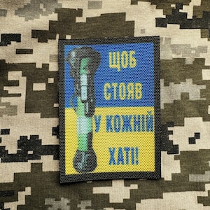 Könnte beinhalten: Ein schwarzer Patch mit einem ukrainischen Flaggen-Design in Gelb und Blau. Der Patch zeigt ein Cartoon-Bild eines Molotow-Cocktails mit dem Text "щоб стояв у кожній хаті!" was übersetzt "Damit es in jedem Haus steht!" bedeutet.