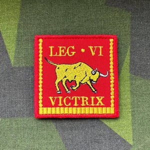 Puede incluir: Un parche bordado rojo con un toro amarillo y el texto "LEG VI VICTRIX".
