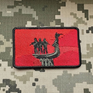 以下が含まれることがあります： 赤い刺繍のパッチ。黒いシルエットで、4人の人物が龍の頭を持つ船の上に立っている。