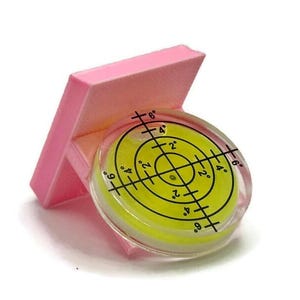 May include: A pink plastic level with a yellow circular bubble level. The bubble level has black markings indicating degrees from 2 to 6. The bubble level is labeled with the text "+6°", "+4°", "+2°", "2°", "4°", "6°", "9°", "9°".