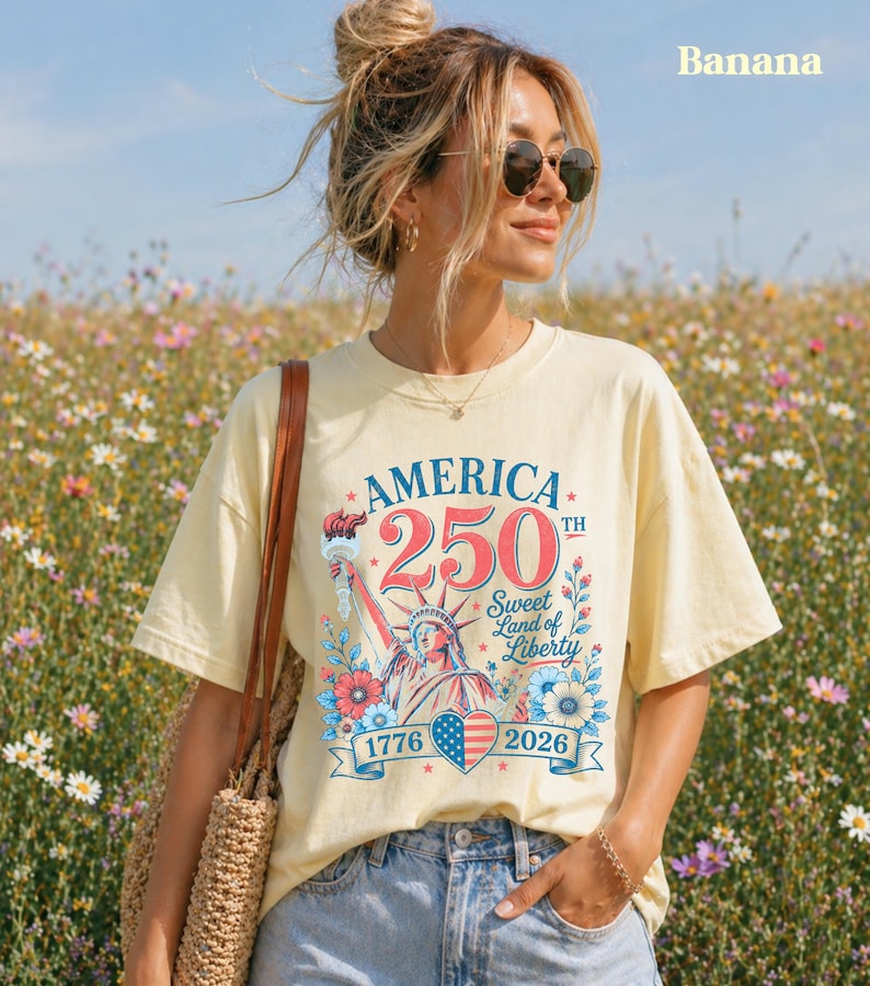K&ouml;nnte beinhalten: Hellgelbes T-Shirt mit einem patriotischen Design zum 250. Jahrestag Amerikas. Die Grafik zeigt die Freiheitsstatue, florale Elemente und den Text "America 250th Sweet Land of Liberty 1776-2026."
