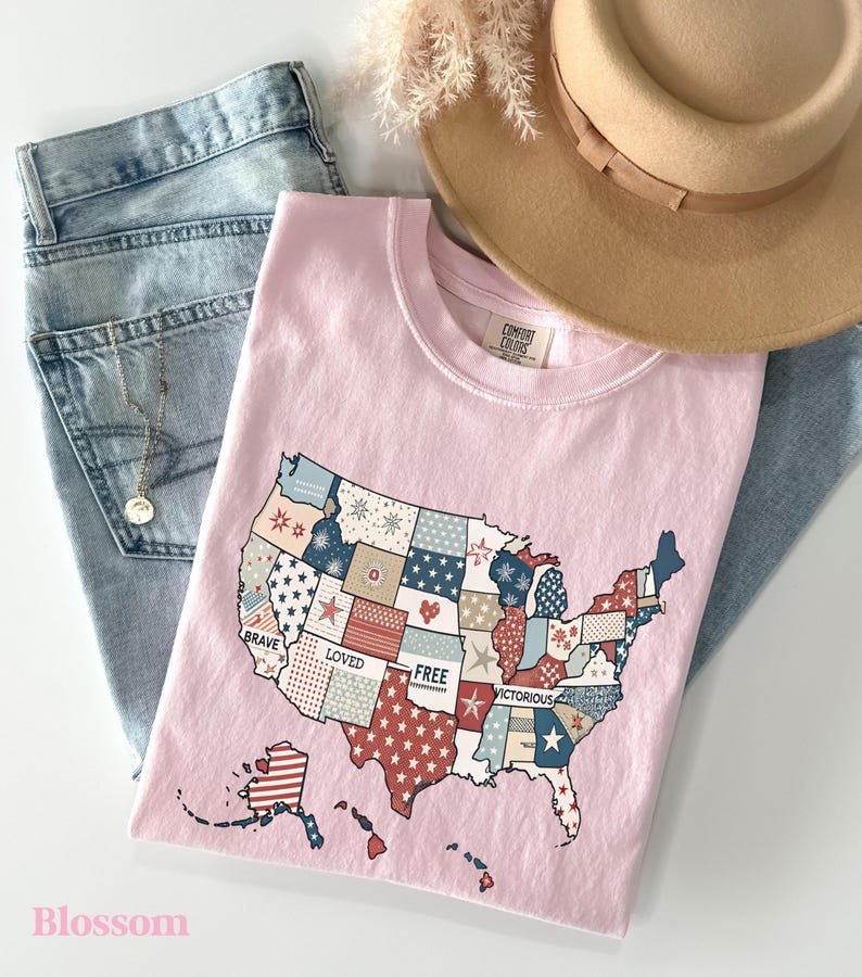May include: Pink t-shirt with a patchwork design of the United States map. The map is made up of different colored squares with stars and stripes. The words "Brave", "Loved", "Free", and "Victorious" are printed on the map.