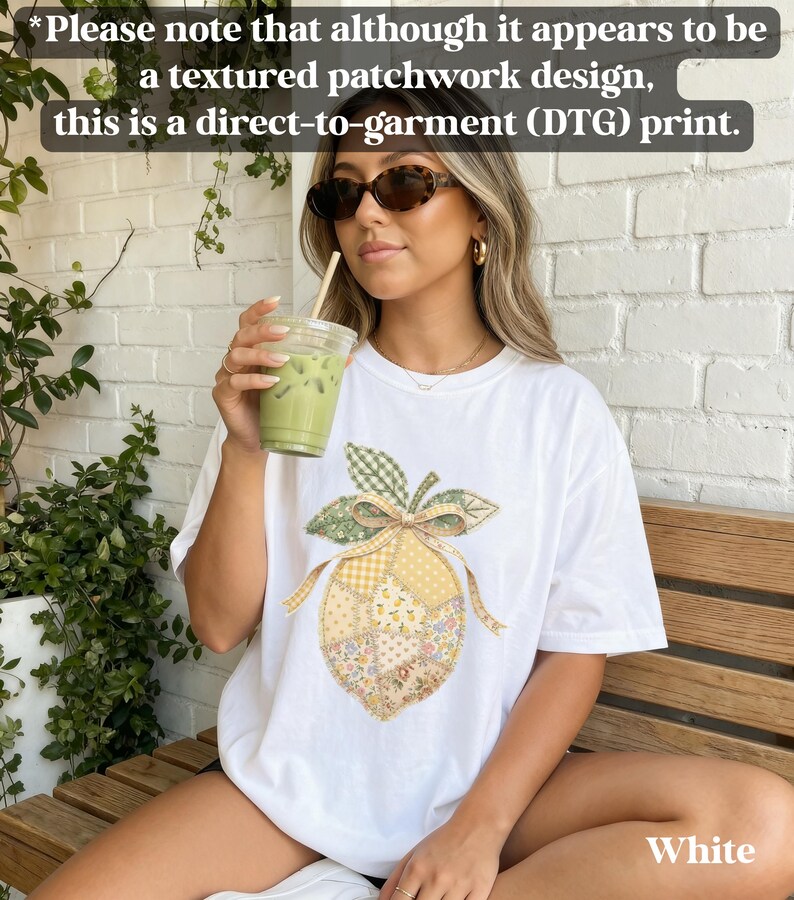 May include: White t-shirt with a direct-to-garment print of a lemon with a patchwork design. The lemon has a green leaf and bow, with yellow and floral patterned sections. The text on the shirt says "White".